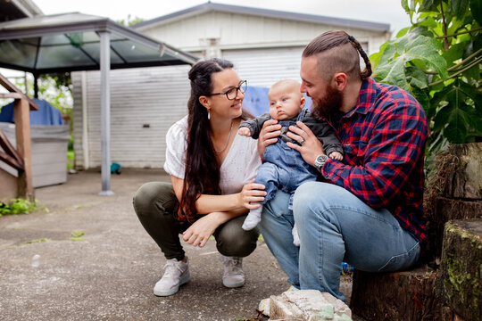 Dad sitting on wooden block holding baby boy with mum squatting beside them