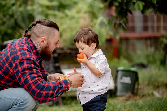 Toddler boy eating half of an orange while dad crouching holding the other half