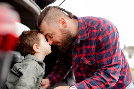 Father leaning forward touching foreheads with son seated on car boot