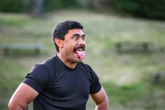 Samoan man standing with arms on his waist sticking his tongue out in a grassy field
