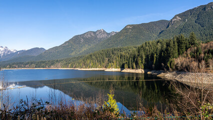 Fototapeta premium Capilano lake - tranquil waters and scenic snow capped mountain view, north Vancouver