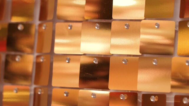Close-up view of a decorative wall made of small reflective metallic tiles arranged in a geometric grid pattern. 