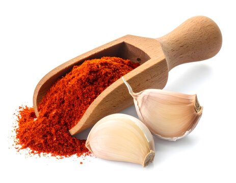 Wooden scoop of red chili powder with sliced garlic on white background