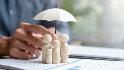 Life insurance concept showing family figures protected under umbrella on policy documents. Represents coverage, beneficiaries, financial security, dependents protection, long-term planning. © Garun Studios