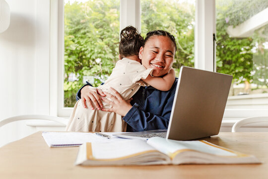 Toddler girl hugging teen sister while doing her homework