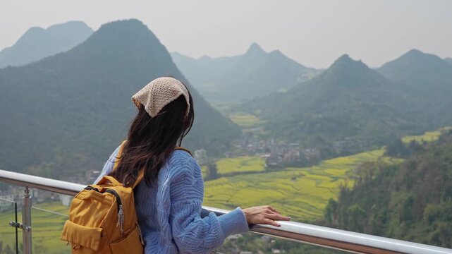 Young happy woman tourist enjoying the canola fields with mountain views while traveling in Luoping, China