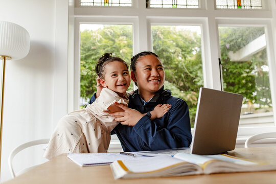 Toddler girl hugging teen sister while doing her homework