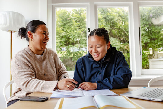 Samoan mum helping teenage daughter with her school workbook