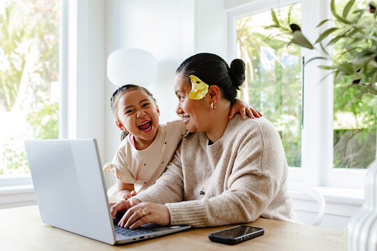Young girl laughing with mum while working on her laptop