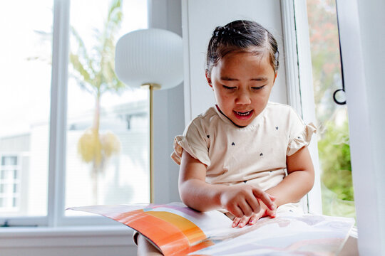 Young samoan girl reading a book while sitting by the windowsill