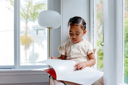 Young samoan girl reading a book while sitting by the windowsill
