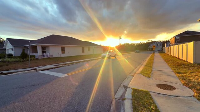 Slow walking video through a quiet suburban neighborhood at sunset with residential homes, parked cars, sidewalks, and warm evening light creating a calm lifestyle atmosphere.