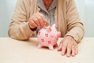 Retired elderly woman putting coins money in piggy bank and worry about monthly expenses and treatment fee payment.