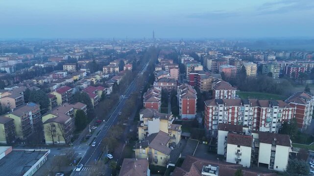 Aerial drone view captures Viale Po cutting through residential districts of Cremona, Lombardy, Italy, with the Torrazzo di Cremona and Duomo di Cremona visible under hazy winter weather.