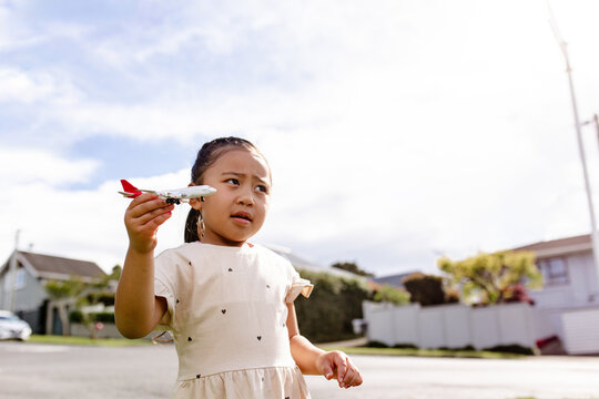 Young Samoan girl holding a toy aeroplane up in the air outdoors - travel concept