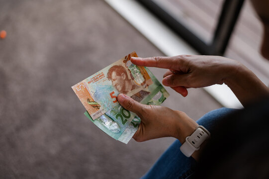 A person sorts through New Zealand notes while seated on a soft surface in a cosy room