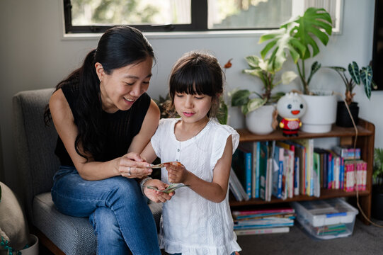 A mother shows different New Zealand banknotes to her young daughter in a living room