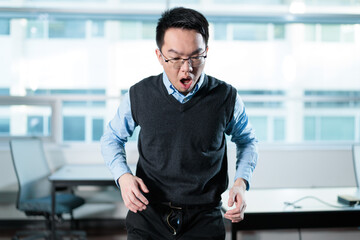 A surprised young man looks down embarrassed after discovering his pants zipper is open in a modern office, ideal for workplace mishaps, embarrassing moments, or wardrobe malfunctions concepts. © fotolite