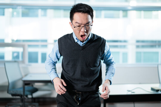 A surprised young man looks down embarrassed after discovering his pants zipper is open in a modern office, ideal for workplace mishaps, embarrassing moments, or wardrobe malfunctions concepts.