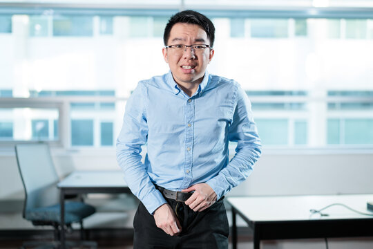 Young Asian professional zipping pants up with an embarrassed expression in an office, ideal for workplace mishaps, embarrassing moments, or office humor concepts.