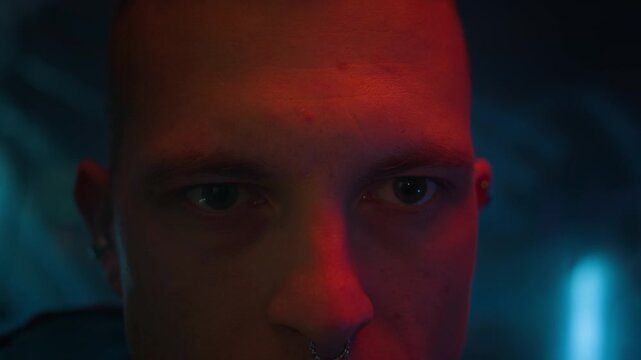 Close up shot of young Caucasian man with nose piercing standing in dark neon room