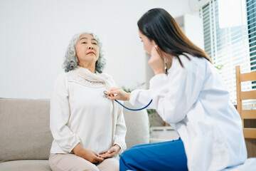 Obraz premium Healthcare professional using stethoscope to examine elderly woman at home. Senior medical checkup, heart health, home care, diagnosis, prevention