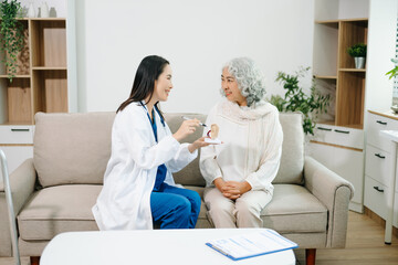 Female doctor explaining ear anatomy to elderly woman during home medical consultation. Hearing...