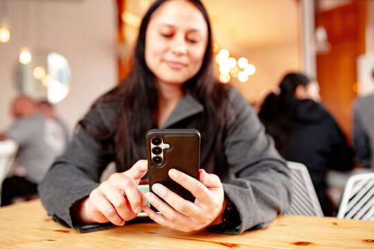 Maori woman sitting at cafe table with a coffee holding her phone