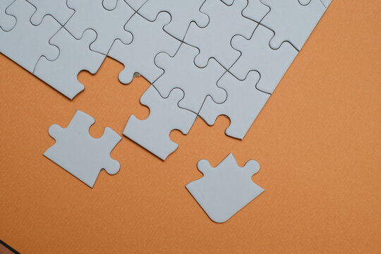 ​A white jigsaw puzzle on an orange background with two missing pieces being placed. Concepts of teamwork, strategy, problem-solving, business solutions and final steps