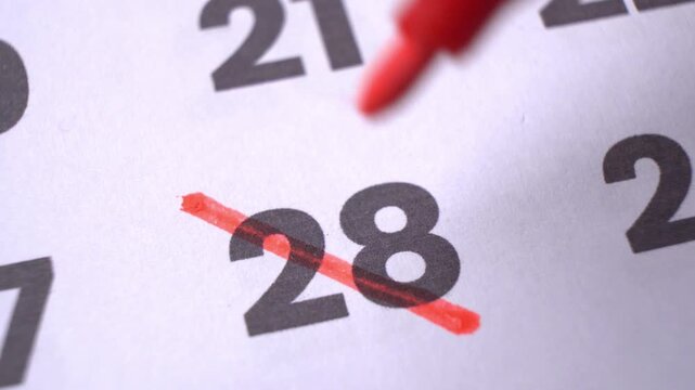 Crossing out calendar dates on a paper schedule close-up, a hand marking off important days and events