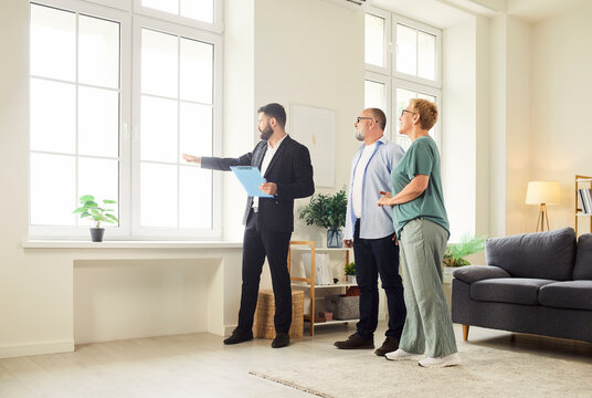 Realtor and agent guide a senior couple through new apartment during a tour and viewing, helping buyers assess the interior and showing key home features. Real estate market and buying property.