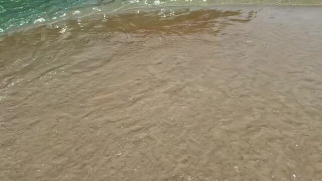 Close up video of bright blue clear waves washing over golden sand on the Andaman Sea coast in southern Phuket, Thailand. Transparent turquoise water and gentle motion highlight tropical shoreline bea