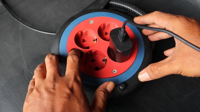 Asian man hand plugging an electrical device into a power extension socket at home. Concept of electricity usage, household energy, power connection, electrical safety, and daily technology use.