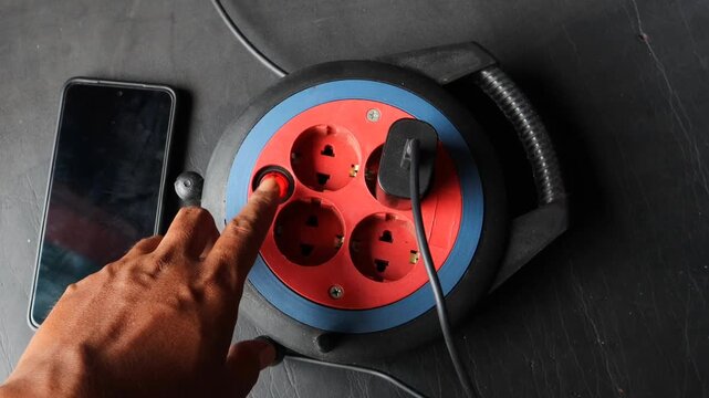 Asian man hand plugging a power adapter into an extension socket beside a smartphone.