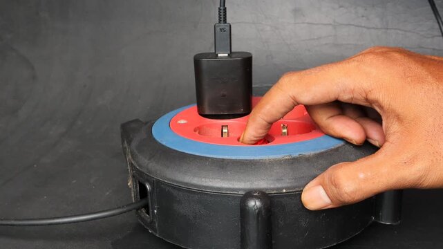 Asian man hand plugging an electrical device into a power extension socket at home. Concept of electricity usage, household energy, power connection, electrical safety, and daily technology use.