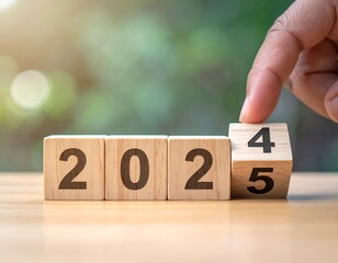 Hand flips wooden cube from 2024 to 2025 on a wooden surface