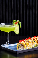 A professional, high-contrast studio shot featuring a gourmet prawn (shrimp) roll served with a side of fries and a vibrant green cocktail on a dark, textured background