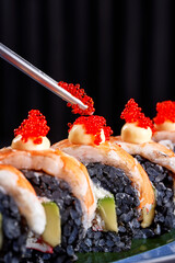 Close-up of premium sushi rolls with black rice, shrimp, avocado, and cream cheese, topped with Japanese mayonnaise and bright red tobiko caviar