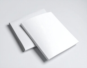 Two stacked, closed, blank white books or magazines lay angled on a light gray surface