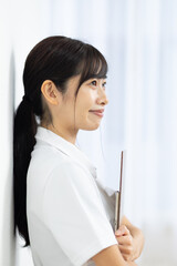 Side View of Smiling Young Woman in White Uniform Holding Clipboard