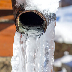 Frozen drainpipe. Icicles cling, snow sits atop. Winter's chill visible in frozen water formations