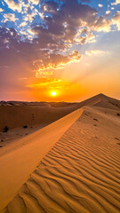 Desert sunset. Golden light shines on a rippled sand dune against a blue, cloudy sky