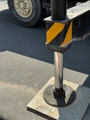 Close-up view of a mobile crane outrigger stabilizer foot placed on a support pad on asphalt road. 