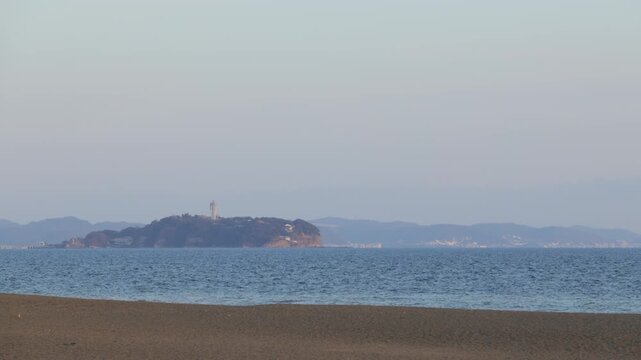 Panoramic view of Enoshima Island from Chigasaki beach at sunset, golden waves and ocean horizon, scenic coastline of Shonan Kanagawa, Japan.