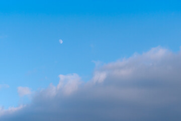 La Lune visible en plein jour dans un ciel bleu nuageux