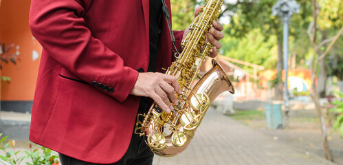 An elegant musician playing a golden saxophone outdoors. Close up.