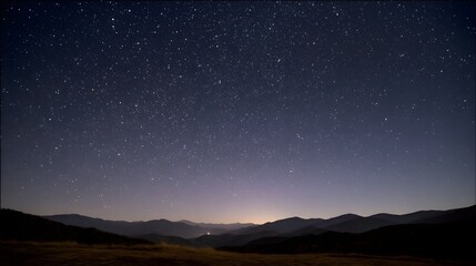Fototapeta premium A vast starry night sky stretches over dark mountain silhouettes with a faint glow on the horizon