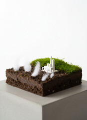 Miniature Factory Emitting Smoke on Mossy Soil Diorama Against White Background