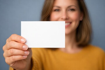 Naklejka premium Business Card Presentation: A woman extends a blank business card, smiling warmly, perfect for showcasing your message, evoking professionalism and connection. 