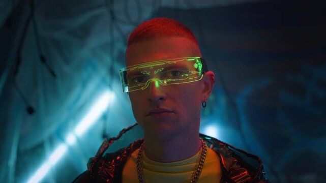 Close up portrait of young cyberpunk man wearing vibrant visor and latex coat looking at camera in neon room